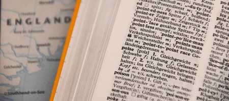 A picture of a dictionary in the word starting with P section, with Poise and Poison visible. Behind it is a map of England.